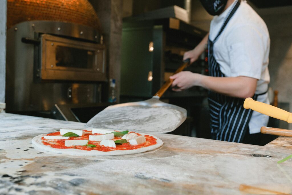 Chef preparing a fresh pizza in a pizzeria kitchen with traditional oven.